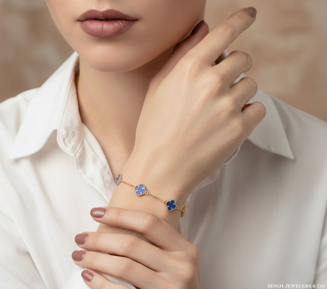Close-up of a hand wearing a gold bracelet with blue flowers, against a neutral background.