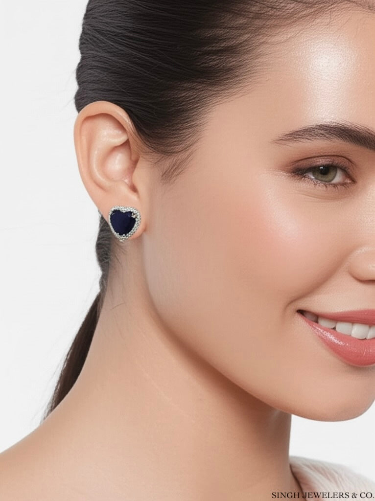 Close-up of a woman wearing a heart-shaped earring with a blue gemstone on a white background.