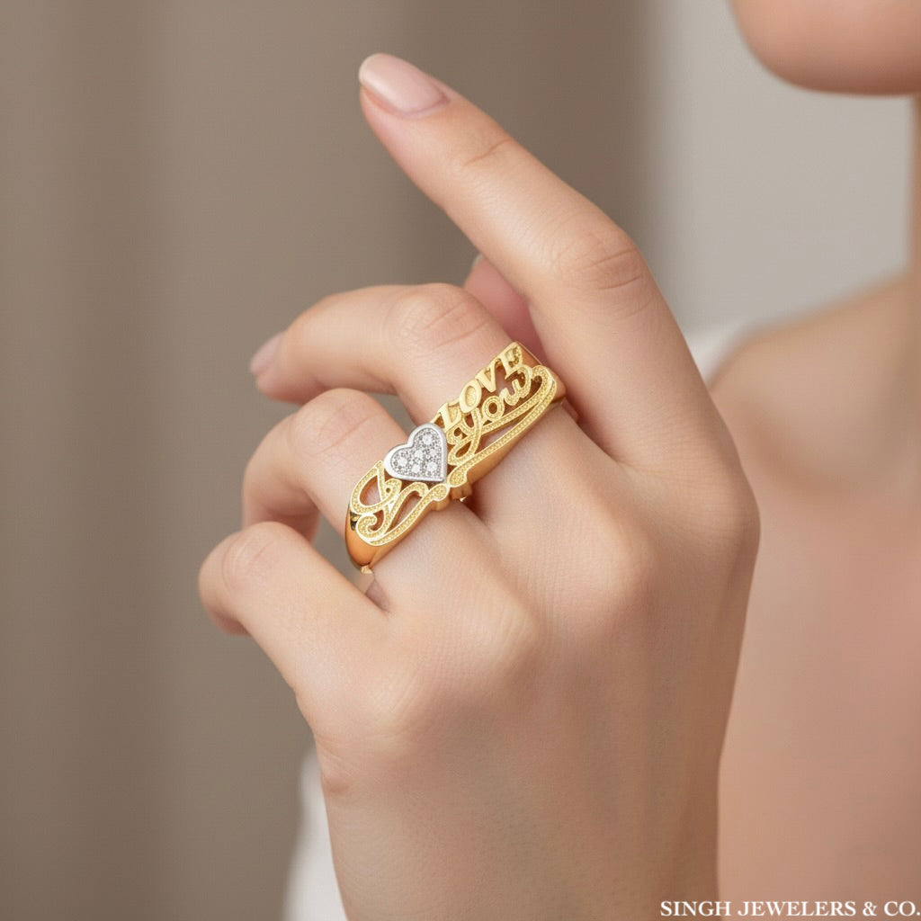 Gold ring with a heart design on a hand, branded 'Singh Jewelers & Co'.