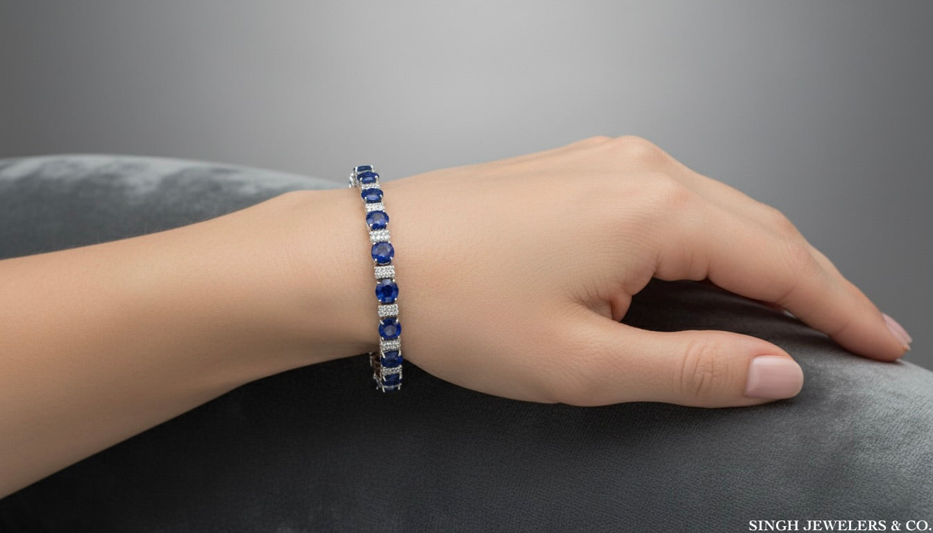 Hand wearing a blue gemstone bracelet on a gray surface with 'Singh Jewelers & Co.' branding.