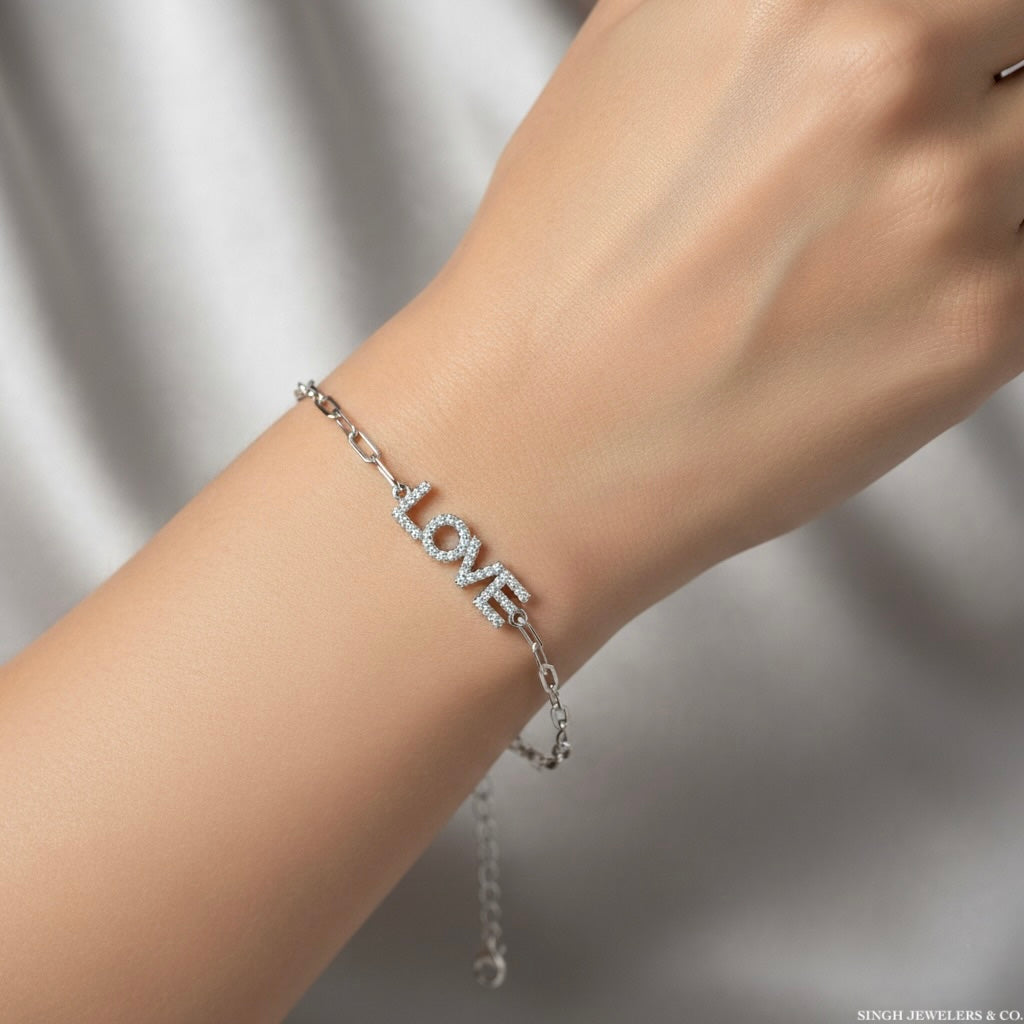 Silver bracelet with 'LOVE' charm on a wrist against a neutral background