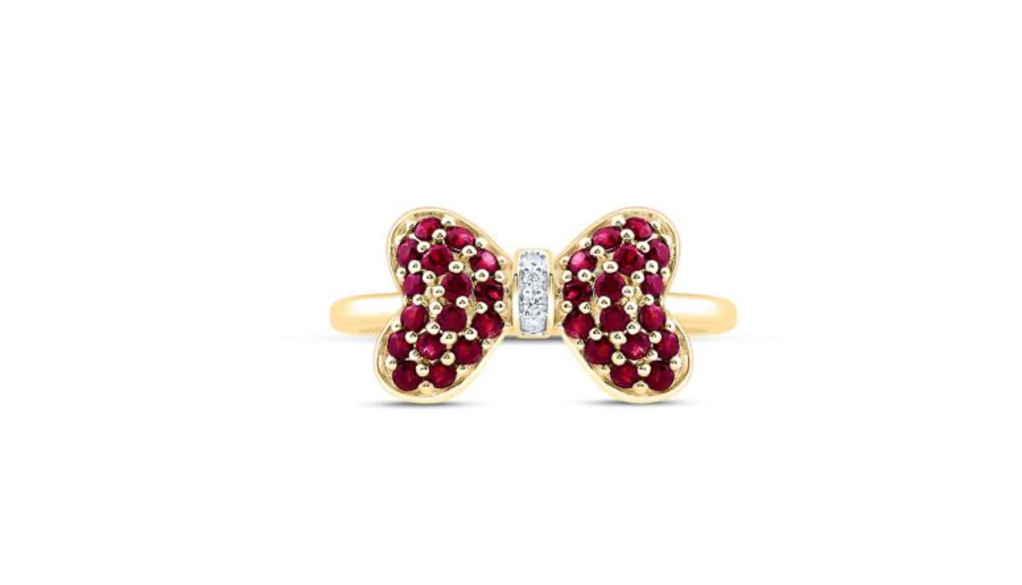 Gold bow-shaped ring with red gemstones and a central diamond on a white background