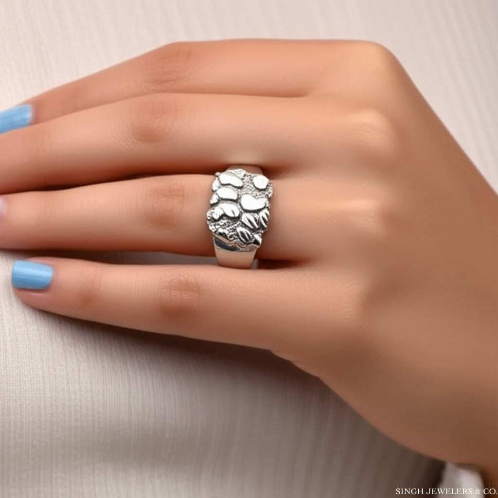 Silver ring on a hand with light blue nail polish against a neutral background