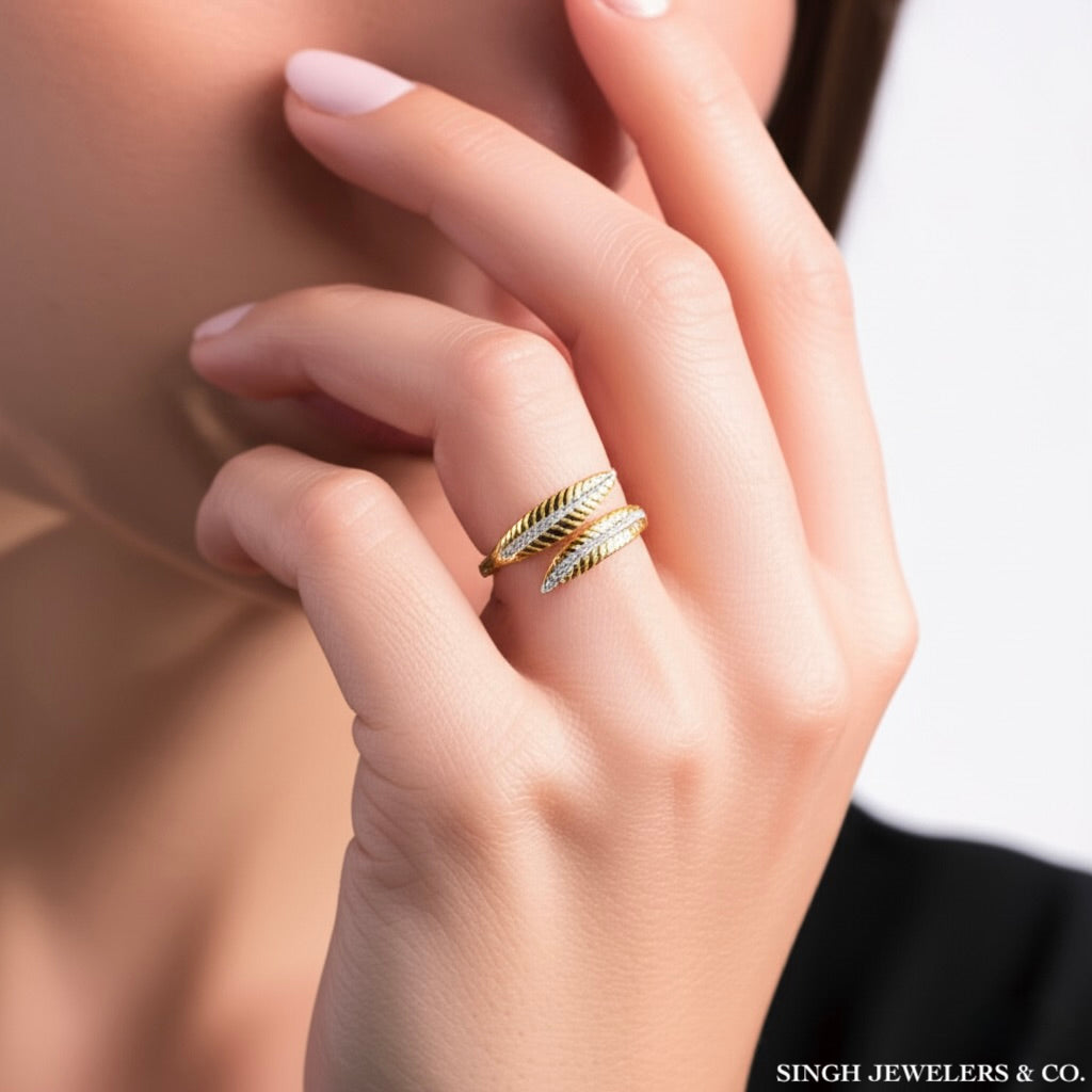 Hand wearing a gold ring with feather design, blurred background
