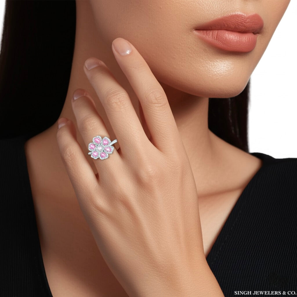 Close-up of a hand wearing a floral ring with pink gemstones, against a neutral background.