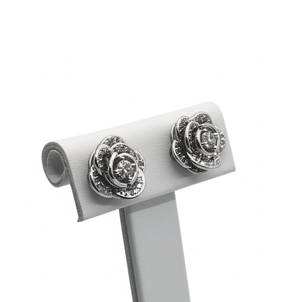 Rose-shaped silver earrings on a white stand against a white background