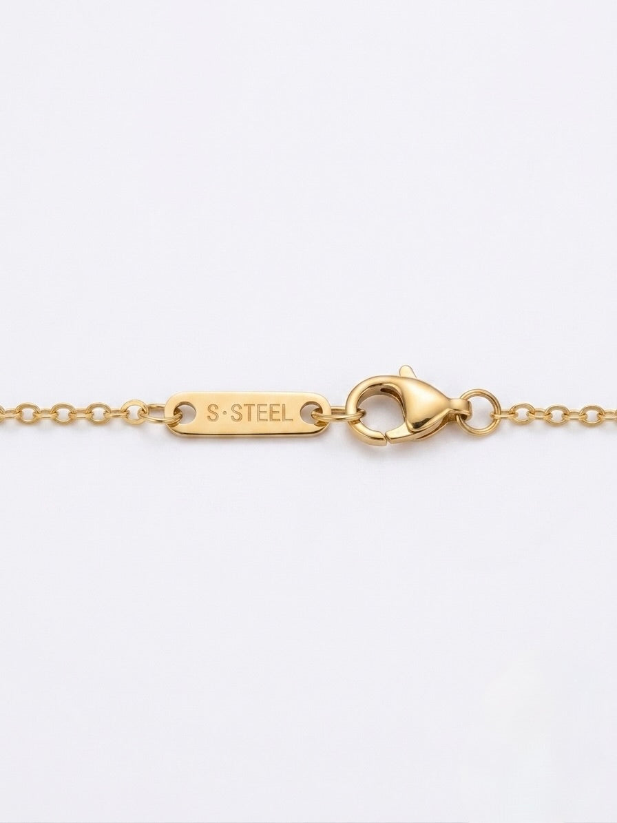 Close-up of stainless steel hallmark stamp next to the clasp on a gold tone heart necklace