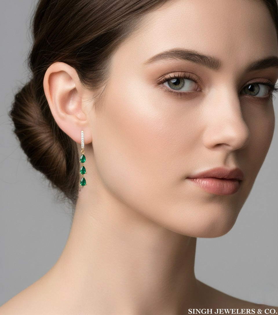 Close-up of a woman wearing emerald green earrings with a gray background