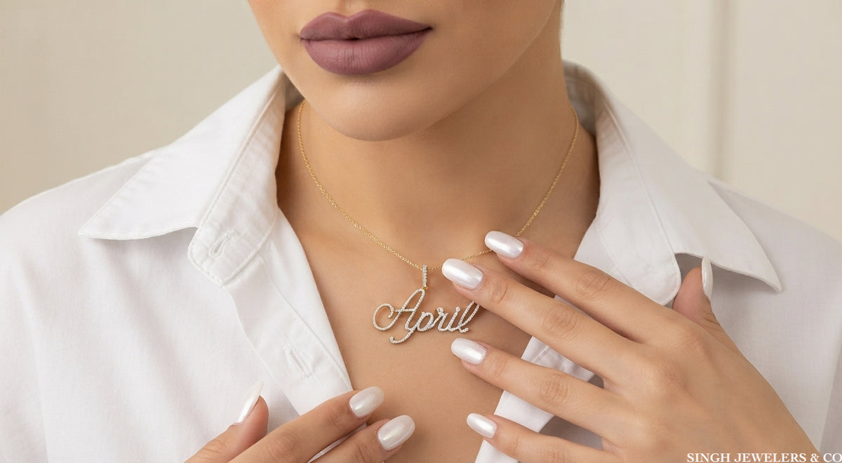 A close-up of a model wearing a delicate gold necklace with a personalized script pendant spelling 'April', styled with a white collared shirt.