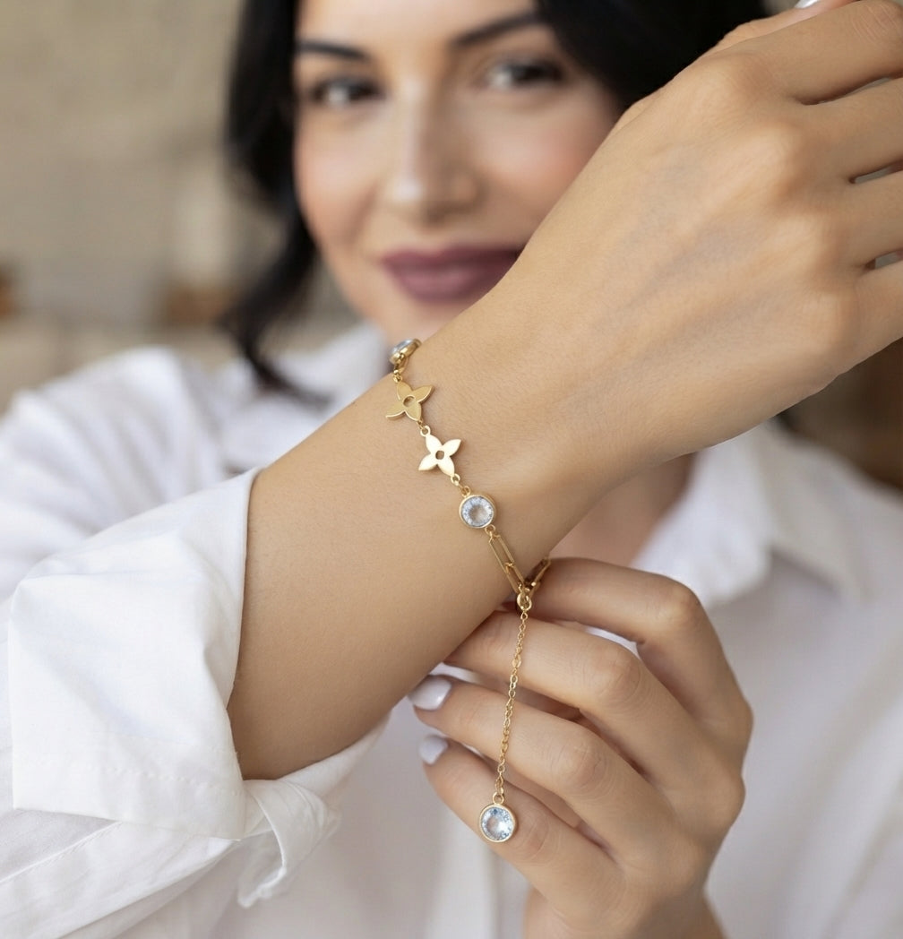 A woman wearing a delicate gold chain bracelet with star and flower charms, featuring clear round stones, shown in a close-up lifestyle shot.