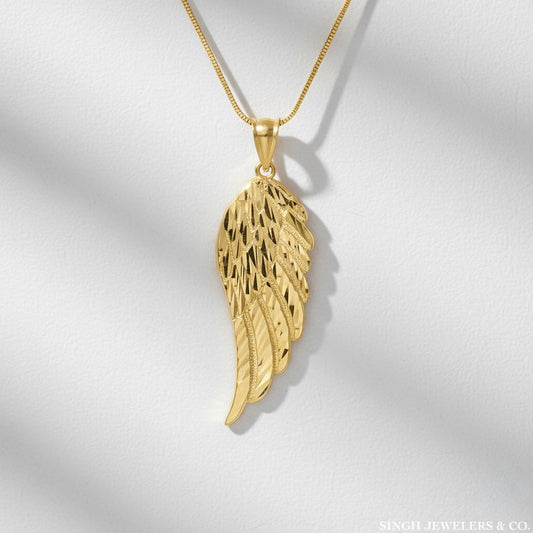Gold angel wing pendant on a chain against a light gray background