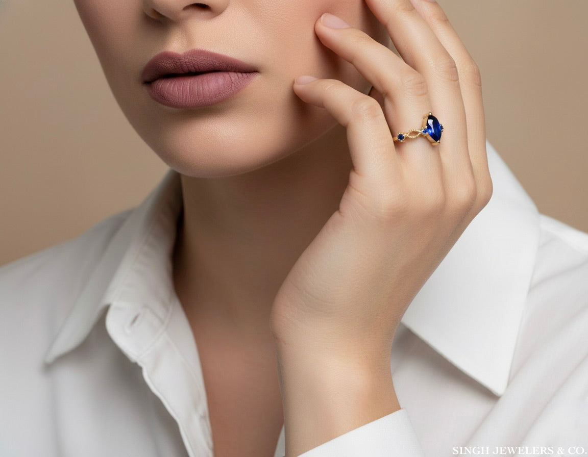 Close-up of a woman's hand wearing a ring with a blue gemstone, against a neutral background.