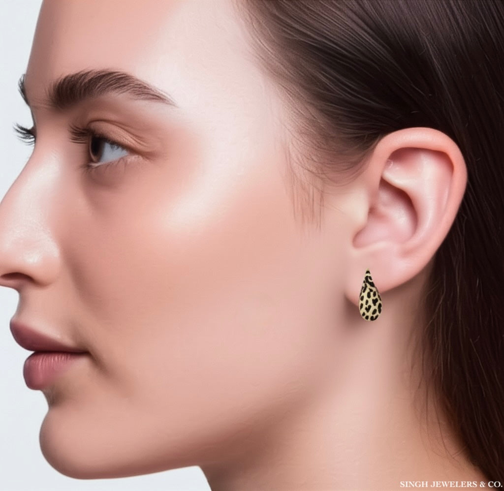 Model wearing teardrop shaped 14K yellow gold earrings with leopard print and black enamel detailing