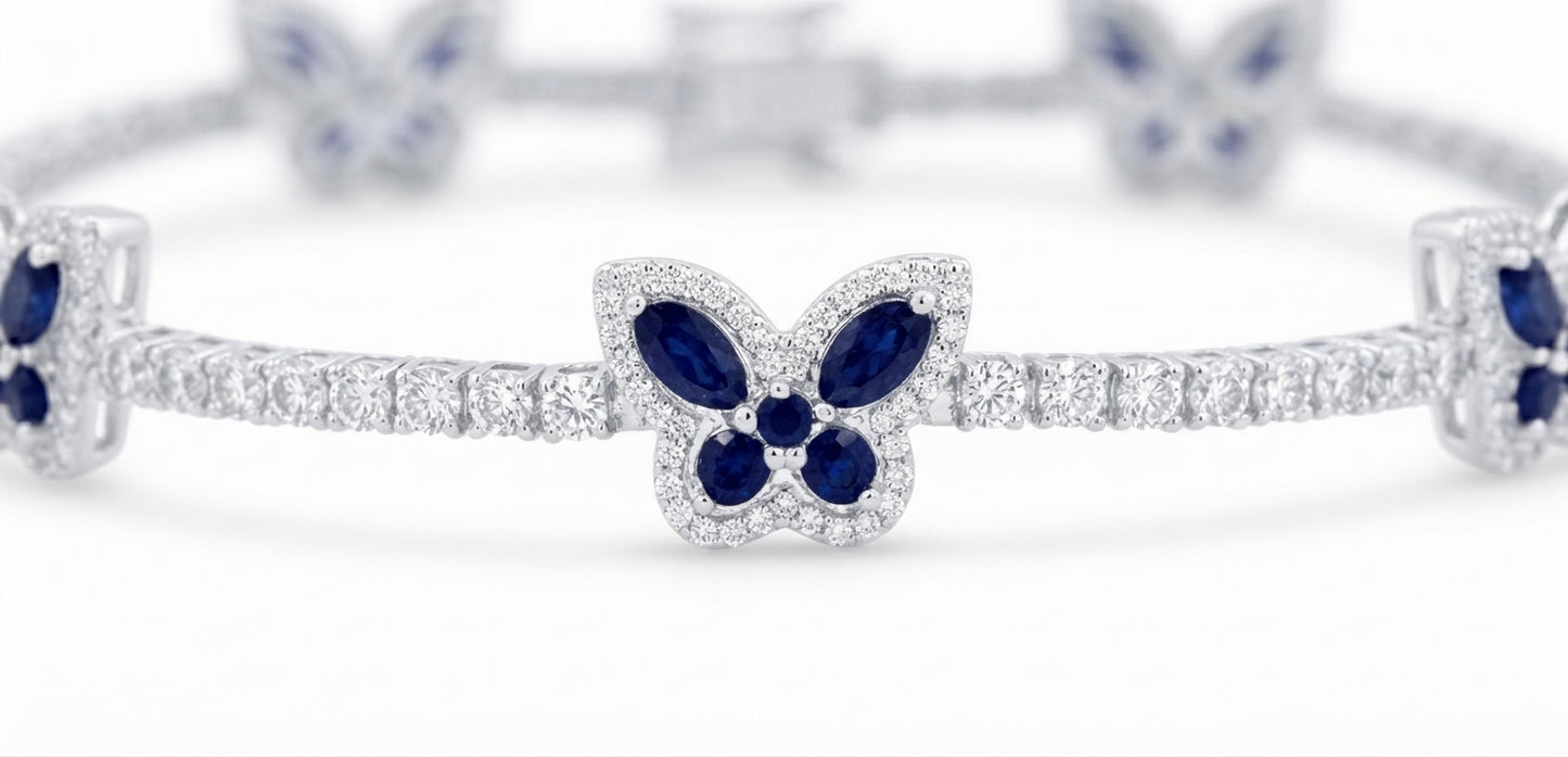 A close-up of a silver-toned bracelet featuring butterfly motifs set with deep blue marquise-cut and round gemstones, accented by pavé-set clear stones, on a white background.