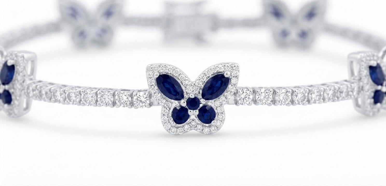 A close-up of a silver-toned bracelet featuring butterfly motifs set with deep blue marquise-cut and round gemstones, accented by pavé-set clear stones, on a white background.