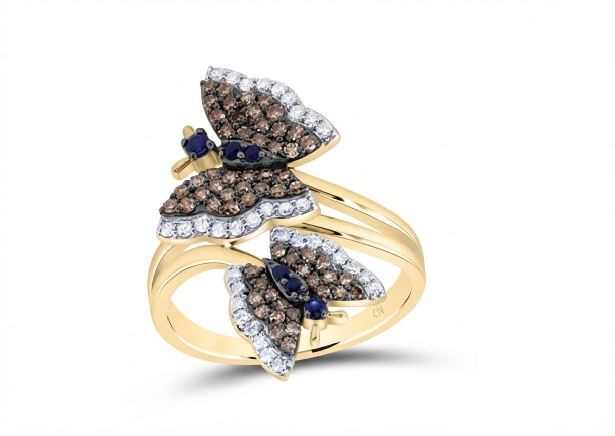 A yellow gold butterfly ring featuring pavé-set brown diamonds on one wing, clear pavé-set diamonds on the other wing, and small dark blue sapphires at the center of both wings, shown on a white background.