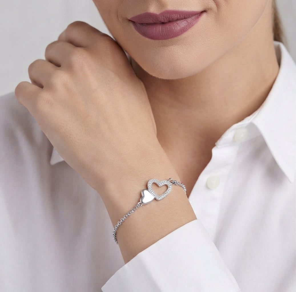 A close-up of a woman wearing a delicate silver chain bracelet with two interlocking open heart charms on her wrist, paired with a white collared shirt.