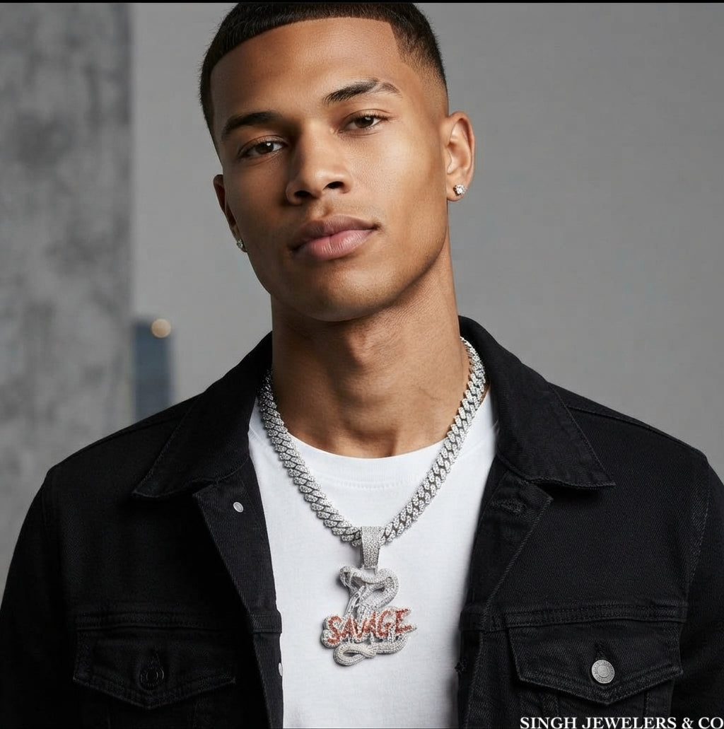 A man wearing a silver chain necklace with a snake pendant engraved with the word 'SAVAGE', styled with a white t-shirt and a black denim jacket.