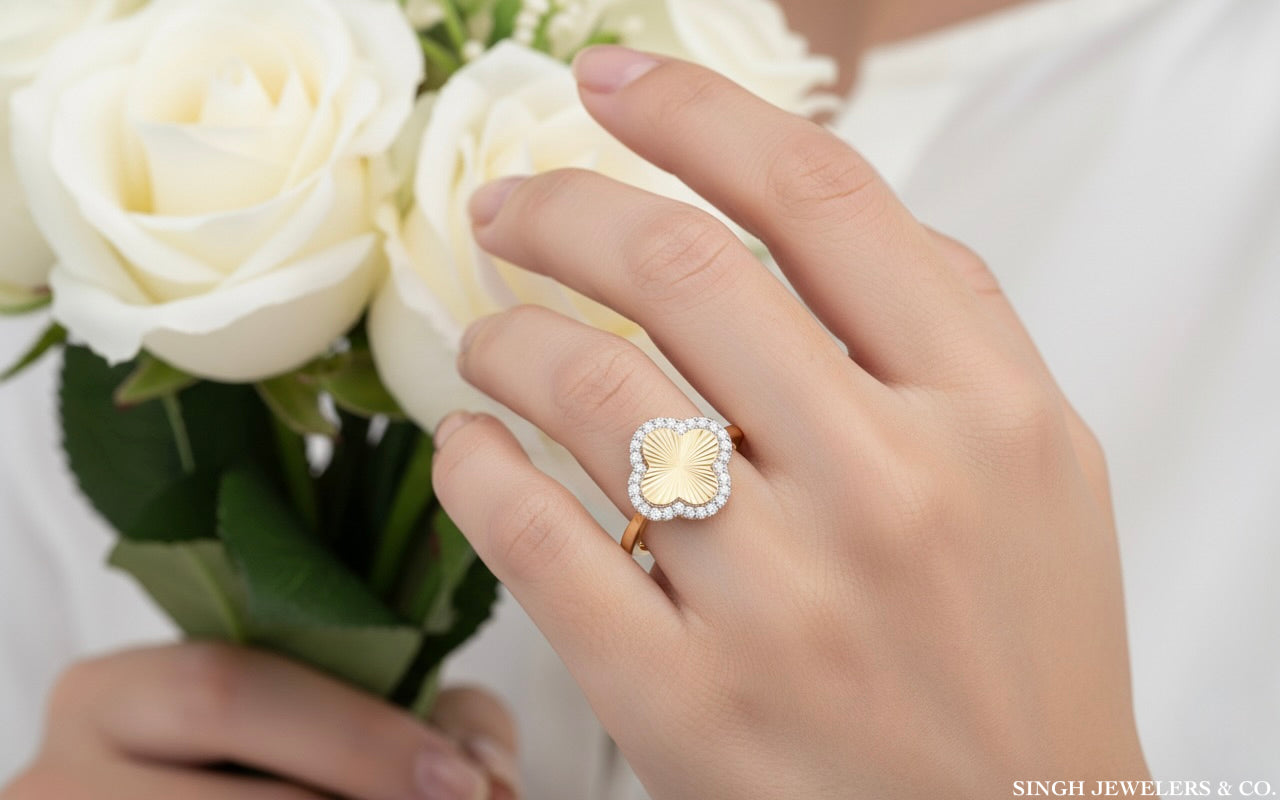 Hand wearing a gold ring with a diamond, holding white roses, with Singh Jewelers & Co. branding.