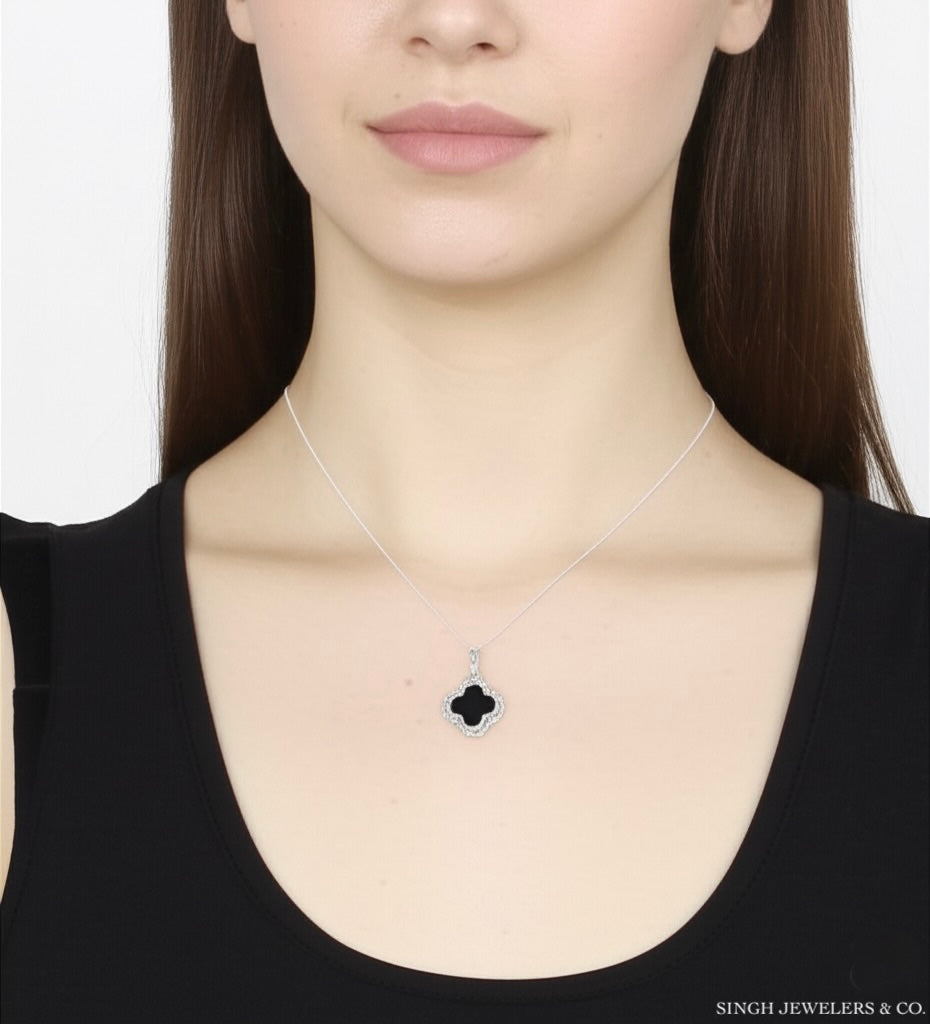 Woman wearing a necklace with a clover-shaped pendant on a plain background