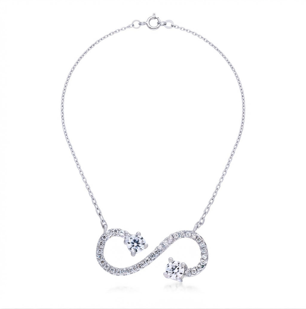 A silver chain necklace featuring a heart-shaped infinity pendant paved with small clear stones, with two small flower-shaped clear stone accents on each loop of the infinity symbol, shown on a white background.